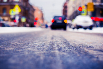 Snowy winter in the big city, the car stopped at red traffic light signal. Close up view from the asphalt level