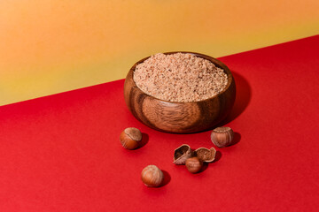 hazelnut flour in a wooden bowl on a red-yellow background with whole nuts in the foreground