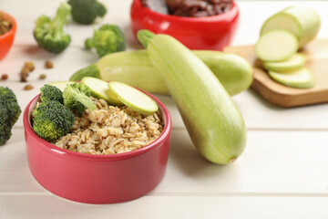 Feeding bowl with oatmeal porridge and vegetables on white wooden table, closeup. Natural pet food
