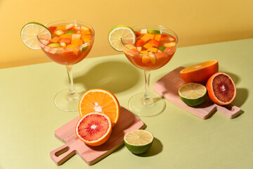 citrus cocktails in glasses on high legs with sliced fruits on a yellow-green background