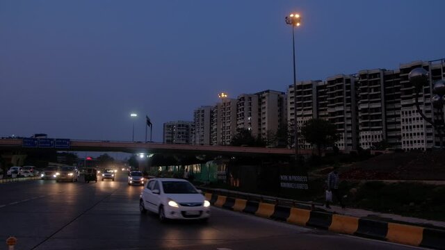 DELHI, INDIA - Mar 15, 2020: Wide establishing shot of major vehicular traffic passing on busy ring-road at AIIMS flyover crossing at sunset dusk, multi storied apartment building