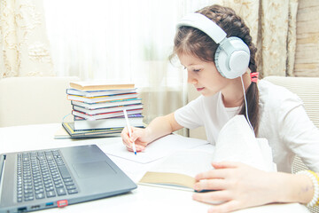 Little Caucasian girl with headphones watching a video tutorial on the computer.