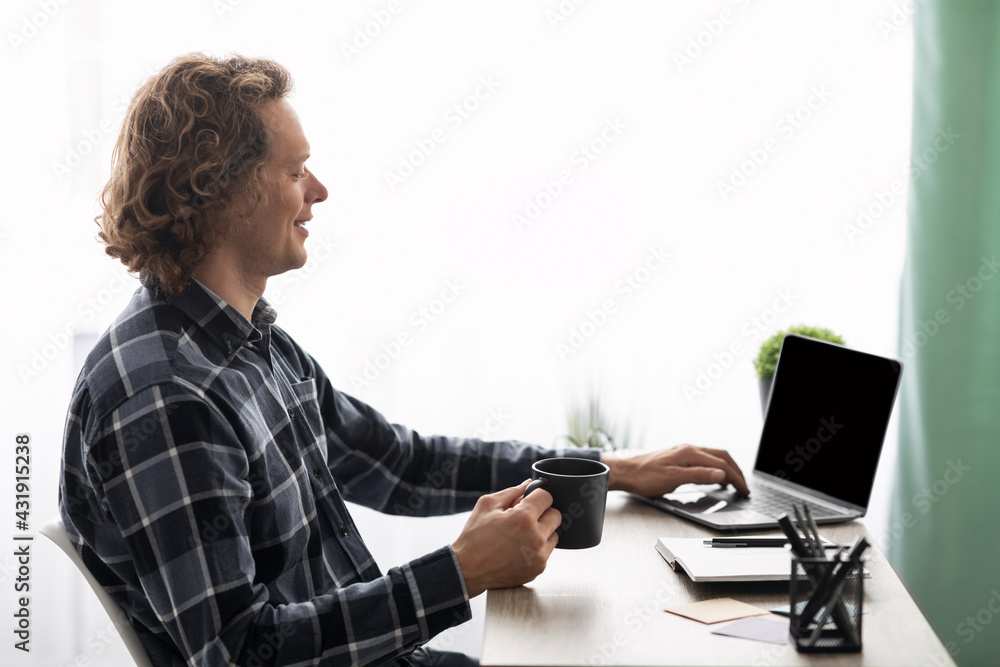 Poster millennial guy using laptop with empty screen at workplace, side-view