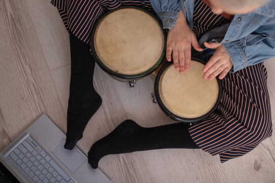 A faceless woman sits on the floor at home and watches educational videos of playing mini bongs. Girl remotely learns to play traditional ethnic drums.