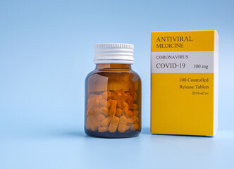 Antiviral medicine COVID-19 tablets in a bottle and box placed on a light blue background. Side...