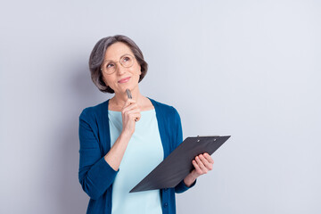 Photo portrait of elder business woman looking empty space keeping pen clipboard isolated on grey...