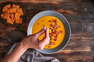 Woman's hand drips green oil from a pipette on traditional pumpkin puree cream soup with carrots,...