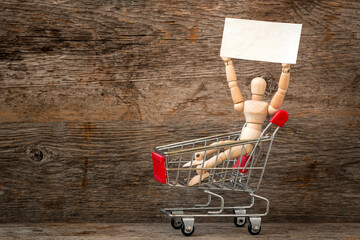 Wooden dummy sitting in a shopping cart and holding blank placard