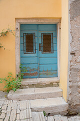yellow facade and blue door with exfoliated paints and weathered stairs.