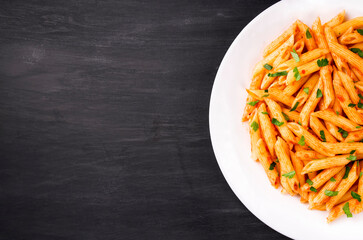 Penne pasta in tomato sauce, decorated with parsley on a black background