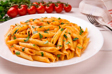Penne pasta in tomato sauce, decorated with parsley on a white wooden table