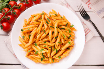Penne pasta in tomato sauce, decorated with parsley on a white wooden table