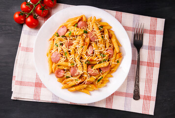Penne pasta in tomato sauce with sausages and cheese, decorated with parsley on a  black background