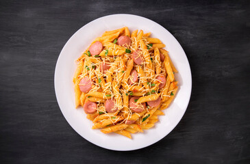 Penne pasta in tomato sauce with sausages and cheese, decorated with parsley on a  black background