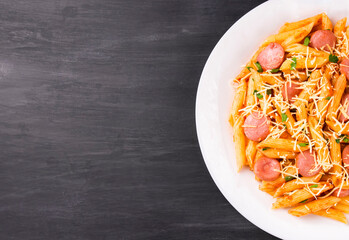Penne pasta in tomato sauce with sausages and cheese, decorated with parsley on a  black background
