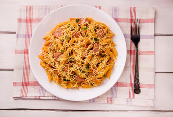 Penne pasta in tomato sauce with sausages and cheese, decorated with parsley on a white wooden table