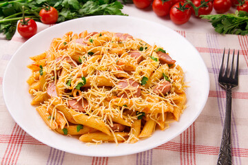 Penne pasta in tomato sauce with sausages and cheese, decorated with parsley on a white wooden table