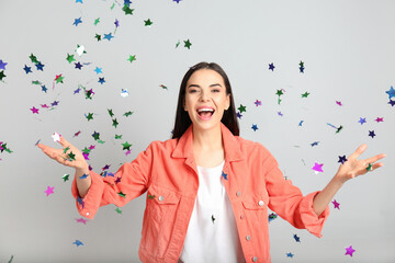 Emotional woman and falling confetti on light grey background