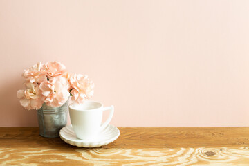 White coffee cup with carnation flower on wooden table. pink background