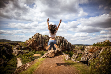 Girl jumping for joy in a spectacular natural mountain landscape with rocks