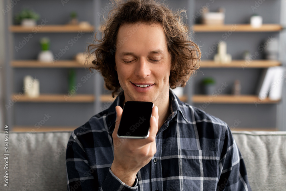 Poster guy using voice assistant on mobile phone sitting at home
