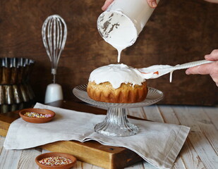 The process of making homemade Easter cakes. A woman spreads whipped cream on baked goods. Brown background in a rustic style