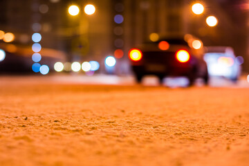 Winter night in the big city, a passing cars on the road. Close up view of snow on the asphalt level