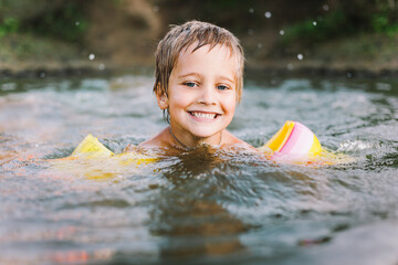 Happy summertime, healthy childhood, sport concept. Close up portrait of little boy smiling and swimming in river in hot summer day. Soft focus. Horizontal shot.