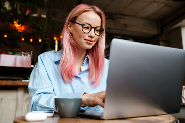 Young smiling woman working with laptop while sitting in cafe