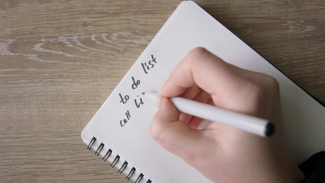 Female hands making list in to do note in notebook. Top shot, close up