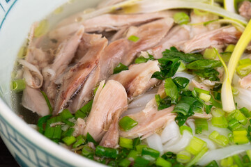 Chicken fillet pieces in soup with rice noodles and chopped greens
