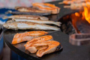 Process of grilling salmon steaks and mackerel fish on black brazier at summer local food market - close up. Outdoor cooking, barbecue, gastronomy, seafood, cookery, street food concept