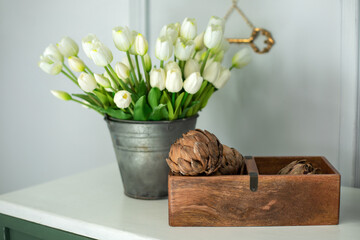 Composition of dried artichoke flowers in wooden box and a bouquet of white tulips in a vase as...