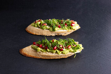 healthy snack - mashed avocado and ripe pomegranate seeds, sesame seeds and aromatic dill, on a black background