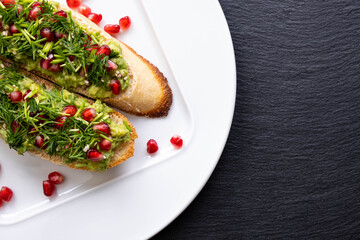 appetizing snacks on a white plate - avocado, sprinkled with ripe pomegranate seeds, sesame seeds and fresh dill