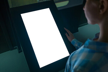 Woman looking at white blank interactive touchscreen display of electronic multimedia kiosk in dark...
