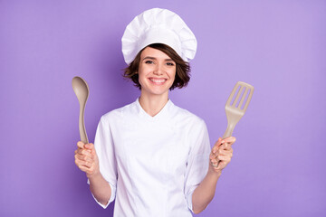 Photo of positive happy nice young woman hold hands kitchenware smile cook isolated on violet color...