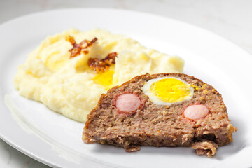 meat loaf filled with egg and sausage served with mashed potatoes and fried onion