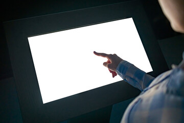 Mockup image - woman touching white empty interactive touchscreen display kiosk in dark room of modern technology museum. Mock up, template, copyspace, education, futuristic and technology concept - obrazy, fototapety, plakaty