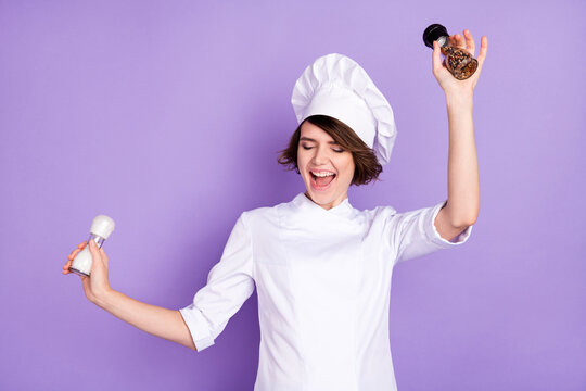 Portrait of attractive funny cheerful chef holding spice bottles dancing good mood cafe isolated over bright violet purple color background