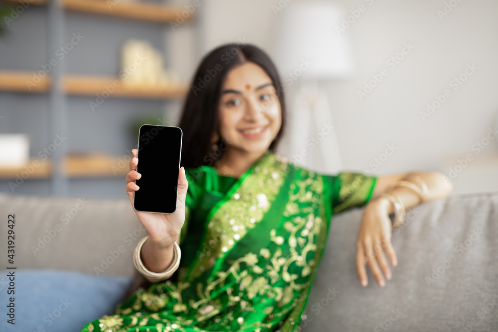 Wall mural Young Indian woman in national sari showing smartphone with blank screen at camera, mockup for website design