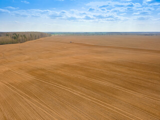 Fototapeta na wymiar Red tractor plows, cultivates a huge field on a spring day with a blue sky. Photo with a drone