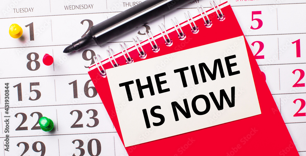 Poster on the calendar is a white card with the text the time is now. nearby is a red notepad and a marker.