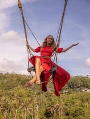 Bali swing trend. Caucasian woman in long red dress swinging in the jungle rainforest. Vacation in...