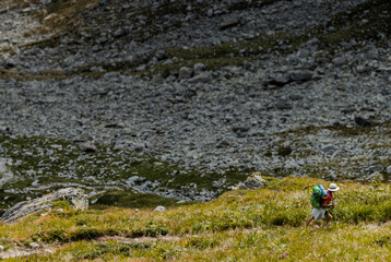 Girl traveler with green backpack and hat walking in the mountains.