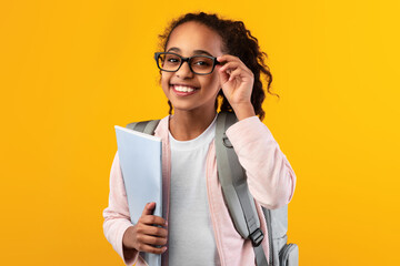 Cheerful young black girl holding textbooks looking at camera