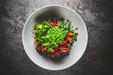 Vegetarian vegetable salad with mushrooms, arugula, tomato, beans and pepper in a bowl on Dark grey black slate background