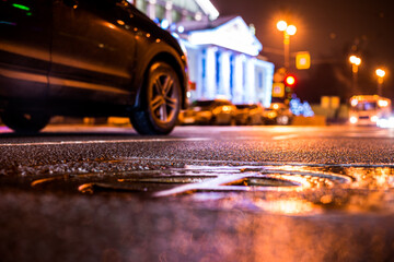 Rainy night in the big city, the car rides near the illuminated luxurious mansion. Close up view of a hatch at the level of the asphalt
