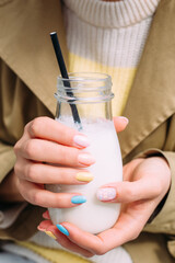  A young woman drinks a milkshake outdoors from a stylish glass jar with a straw