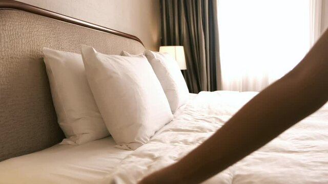 Woman tidy up the bed sheet in hotel room. Room service.